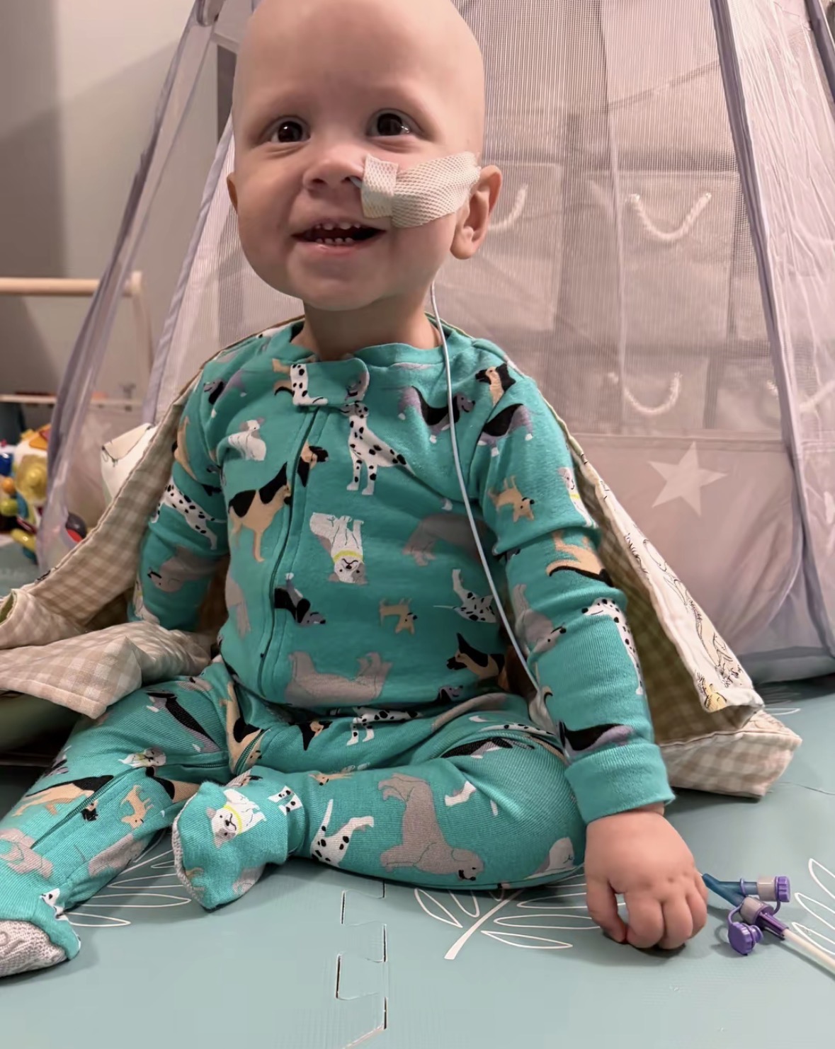 Miguel sorrindo, sentado no tapete com pijama verde